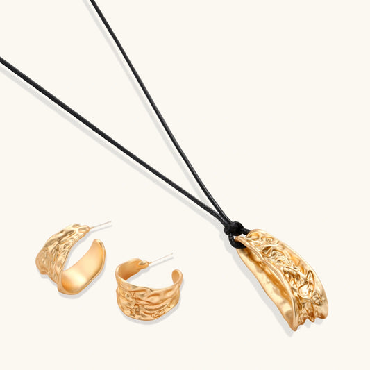Gold-toned textured pendant necklace with matching hoop earrings featuring organic flowing patterns on white background.