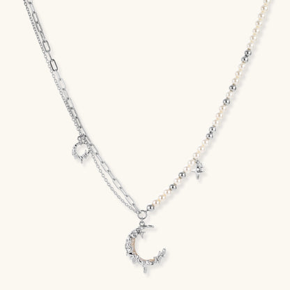 Silver-toned crescent moon pendant with star accents on pearl and chain necklace against white background.