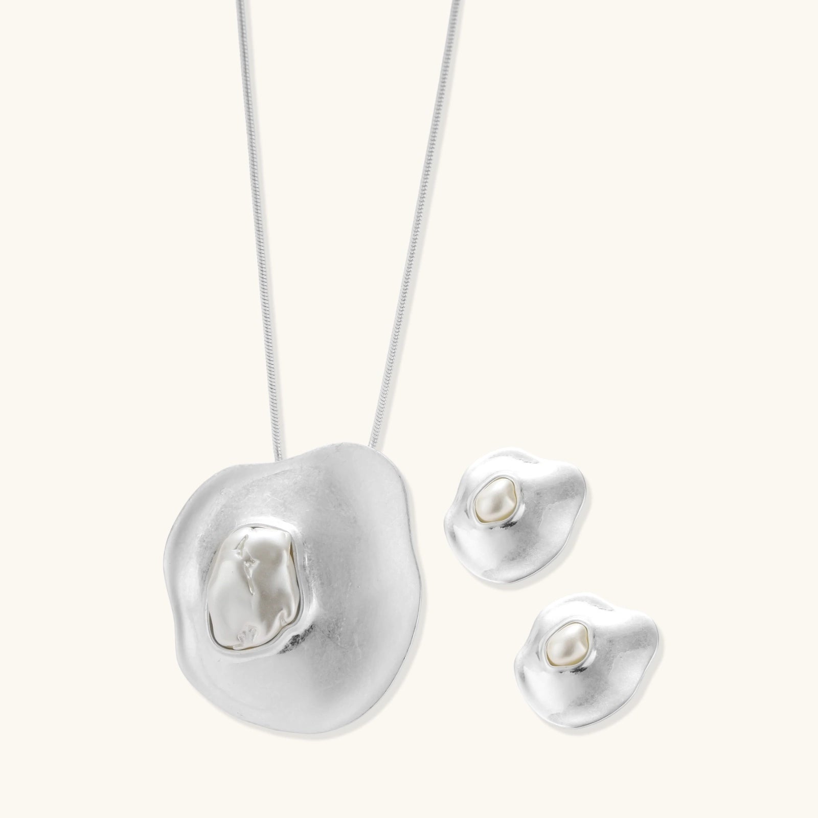 Organic curved earrings and necklace featuring baroque pearls in eco-zinc alloy settings on neutral background