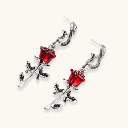 Gothic jewelry set with silver snake designs holding red enamel roses, featuring detailed leaf stems on cream background