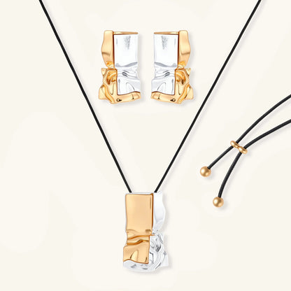 Modern jewelry set with abstract gold and silver pendant on black cord necklace plus matching geometric earrings on white background.