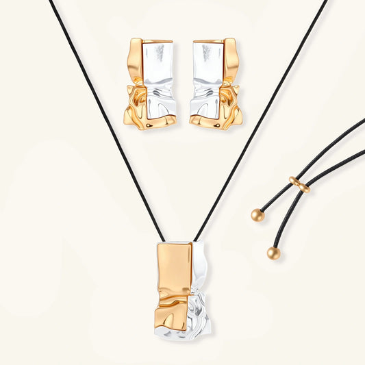 Modern jewelry set with abstract gold and silver pendant on black cord necklace plus matching geometric earrings on white background.