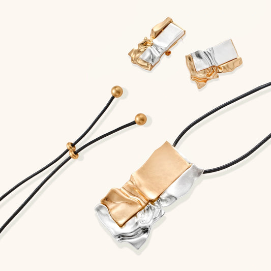 Modern jewelry set with abstract gold and silver pendant on black cord necklace plus matching geometric earrings on white background.