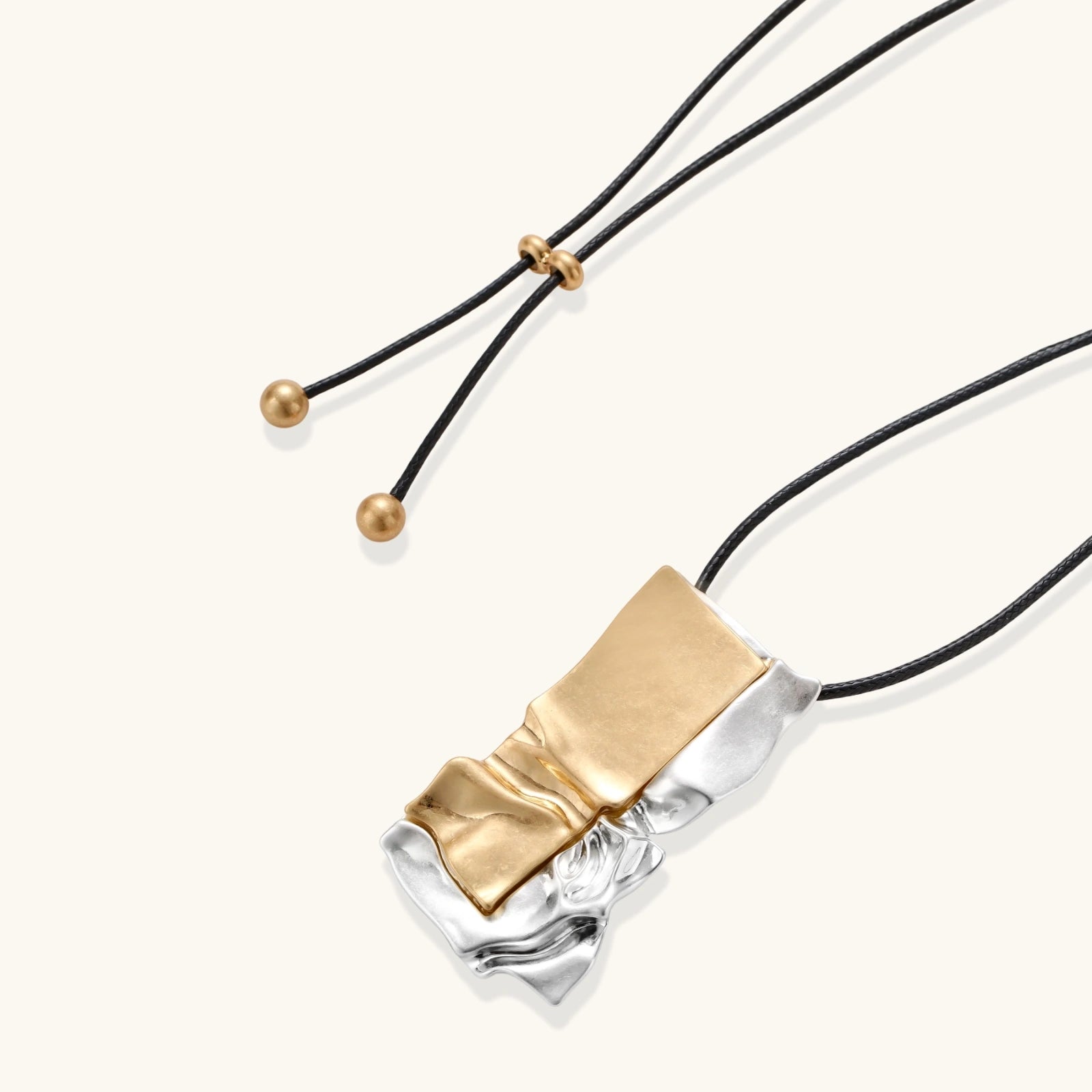 Modern jewelry set with abstract gold and silver pendant on black cord necklace plus matching geometric earrings on white background.