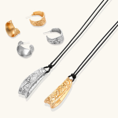 Gold-toned textured pendant necklace with matching hoop earrings featuring organic flowing patterns on white background.