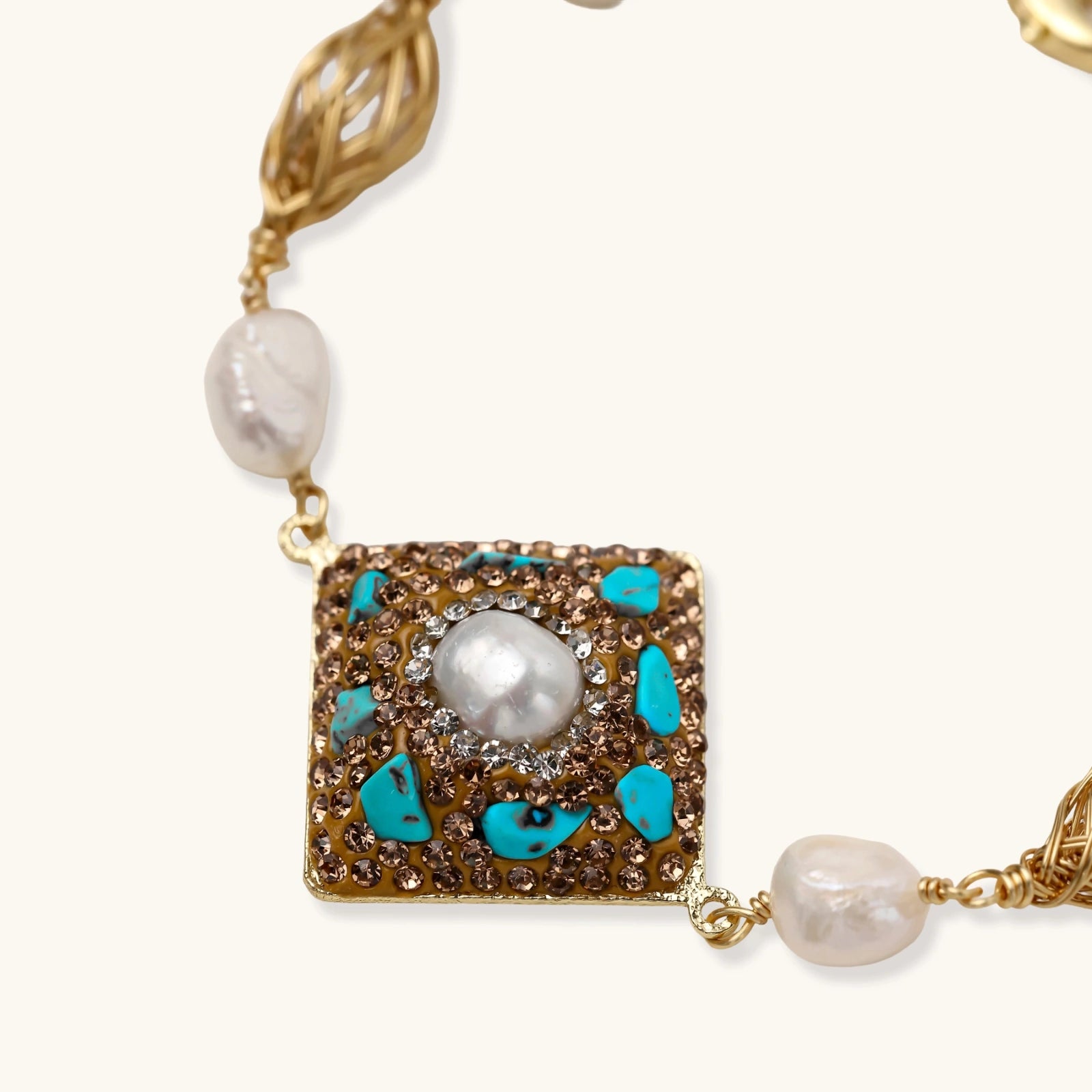 Gold-plated bracelet with baroque centerpiece, turquoise stones, freshwater pearls, and ornate chain links on cream background.