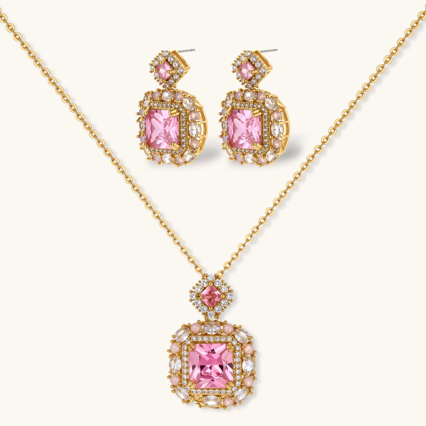 Ornate gold-plated jewelry set with rose pink zirconia center stones and crystal accents on cream background.