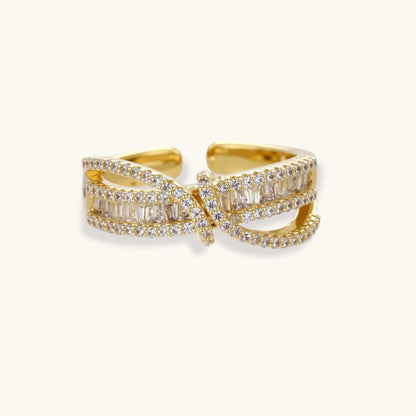Close-up of gold-plated adjustable ring with crossing bands and sparkling zirconia stones on white background.