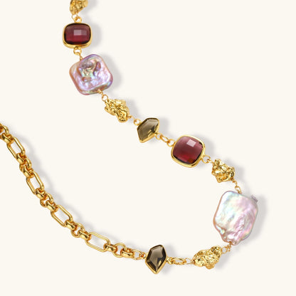 18k gold-plated chain necklace with iridescent baroque pearls and burgundy gemstones on white background.