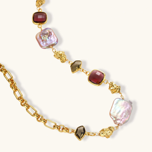 18k gold-plated chain necklace with iridescent baroque pearls and burgundy gemstones on white background.